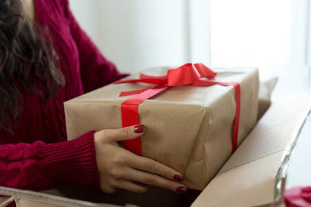 A woman removing a generically wrapped present from a cardboard box.